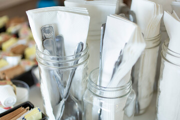 A view of several large mason jars filled with silverware and napkins, in a restaurant setting.