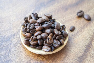 Artistic composition in natural sunlight. Coffee beans in a small plate of light wood, against a dark wood texture background