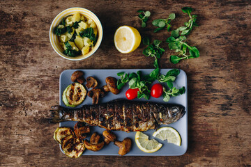 Top view - Grilled trout fish with lemon, herbs, mushrooms and tomato on wooden table