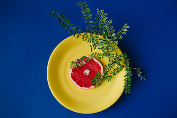 Sliced grapefruit with leaves in yellow plate with blue background