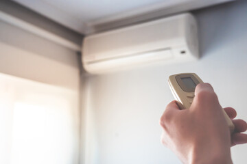 Hand with air conditioner remote control changing the home temperature. Photo with selective focus. 