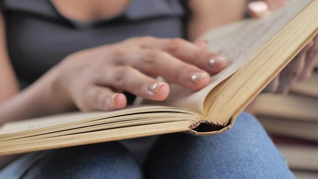 A woman's hand holds a book and moves her fingers along the page while reading. Hand and book: reading a book and holding your fingers along the lines. The reader of the book holds 4k