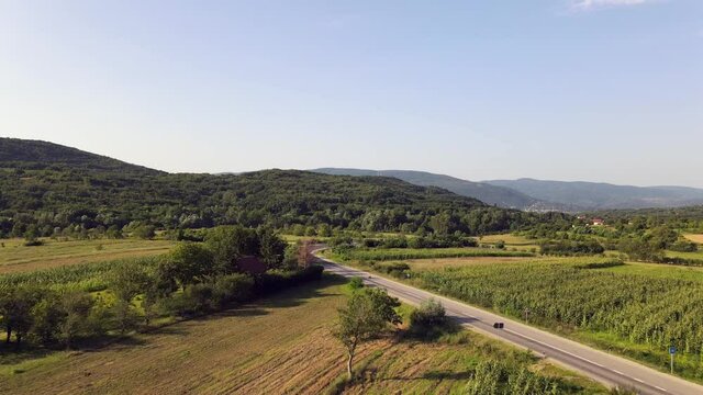 aerial  drone view on curve on the road with trees forest and agriculture fields surrounding - travel and nature freedom concept - rural surroundings with village in back in sunny summer day