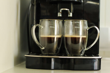 Two glass cups with fresh coffee near coffee machine