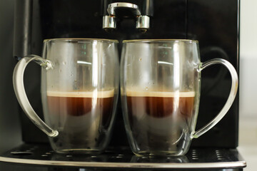 Two glass cups with fresh coffee near coffee machine
