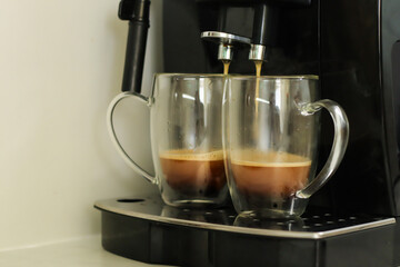 Two glass cups with fresh coffee near coffee machine