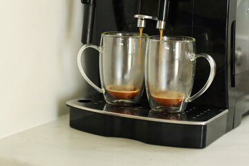 Two glass cups with fresh coffee near coffee machine