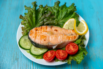 fried red fish, salad, lemon and tomatoes on a plate on a blue wooden table