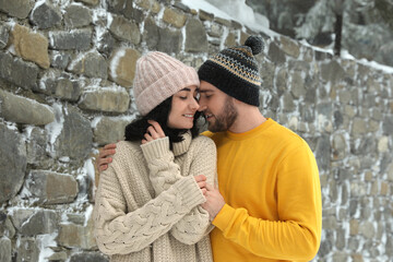 Lovely couple wearing warm sweaters and hats outdoors on snowy day. Winter season