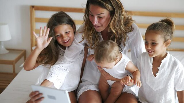 Authentic shot of happy mother with her kids are making a selfie or video call to father or relatives in a bedroom. Concept of technology, new generation, family, connection, parenthood, authenticity