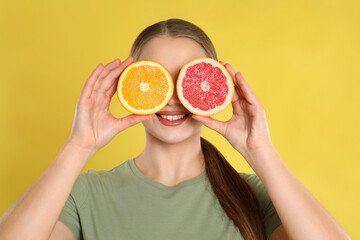 Young woman with cut orange and grapefruit on yellow background. Vitamin rich food
