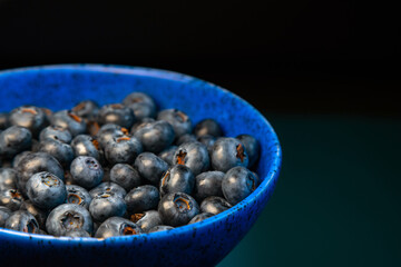 Closeup of ceramic bowl full of blueberries on blue background. Ripe blueberry plate. Organic and healthy food.