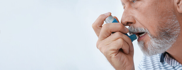 Closeup view of man using asthma inhaler on white background, space for text. Banner design