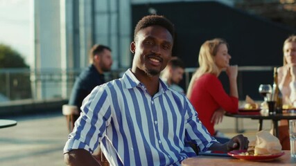 Portrait young african american man sitting looking to camera eating and drinking at street cafe at sunlight face city casual adult outside street serious outdoor slow motion - Powered by Adobe