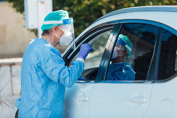 Medical personnel wearing a PPE, performing PCR on a patient inside the car to detect if he is infected with COVID-19