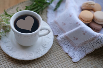 tea in a white cup, macaroni cakes in a wicker plate with a napkin, white flowers, concept of summer tea on the terrace, herbal drink with yarrow and hibiscus, breakfast