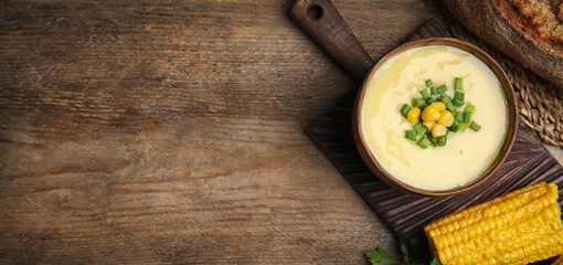 Delicious corn cream soup served on wooden table, flat lay with space for text. Banner design