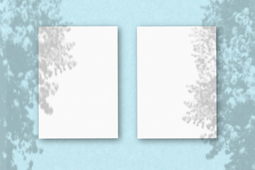 2 vertical sheets of textured white paper on soft blue table background. Mockup overlay with the plant shadows. Natural light casts shadows from an exotic plant. Horizontal orientation