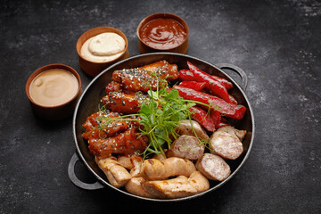 Meat set for beer, sausage, ribs, grilled wings, and three sauces, on a black background