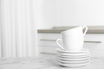 Stack of clean plates and cups on marble table in kitchen. Space for text