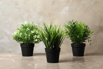 Beautiful artificial plants in flower pots on marble table