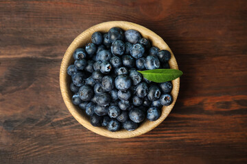 Tasty ripe blueberries in bowl on wooden table, top view