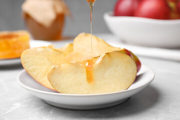 Pouring liquid honey onto apple slices on light grey marble table, closeup. Rosh Hashanah holiday