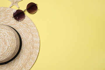 Hat, sunglasses and starfish on yellow background, flat lay with space for text. Beach objects