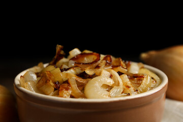 Tasty fried onion in bowl against black background, closeup
