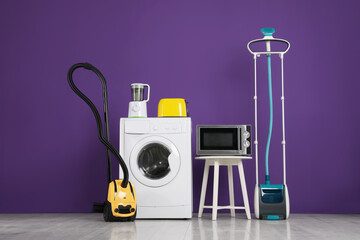 Set of different home appliances with vacuum cleaner on purple background indoors