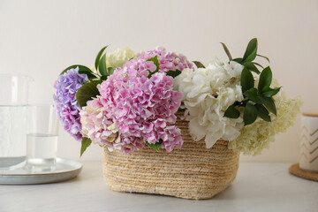 Obraz na płótnie Canvas Beautiful hydrangea flowers in basket on light table, closeup