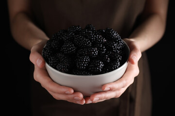 Woman with bowl of fresh blackberries against dark background, closeup