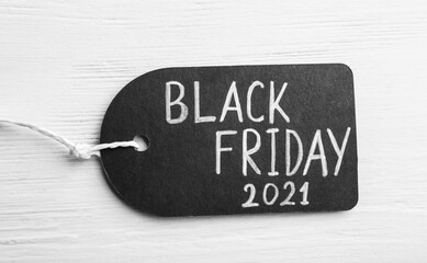 Tag with words BLACK FRIDAY 2021 on white wooden background, top view