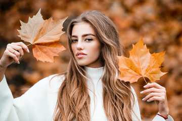 Beautiful girl holds an autumn yellow leaf near the face. Fashion portrait woman hides her face...