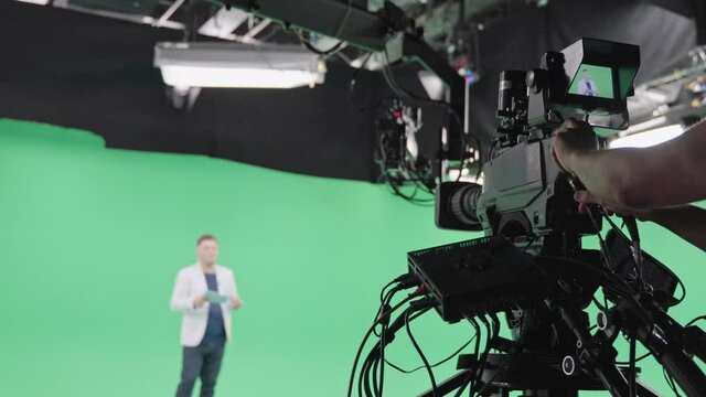 Film crew in green studio shooting video. Chroma - technology of combining two or more images or frames in single composition. Cameraman, director, crew. Filmmaking industry.