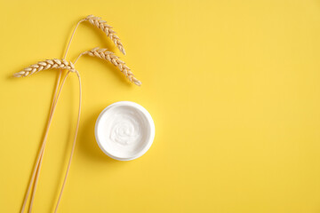 Jar of organic cream with wheat on yellow background. Flat lay, top view, copy space. Natural organic product, beauty and spa concept