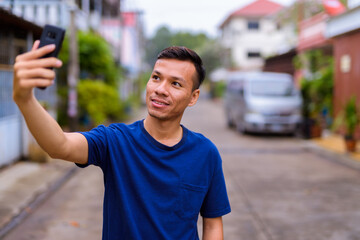 Happy young Asian man taking selfie in the streets outdoors