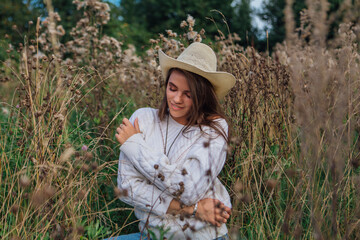 Young beautiful brunette woman sitting on the grass, smiling and touching her hair