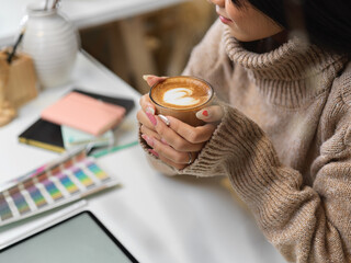 Female in sweater holding a cup of hot latte coffee on office desk