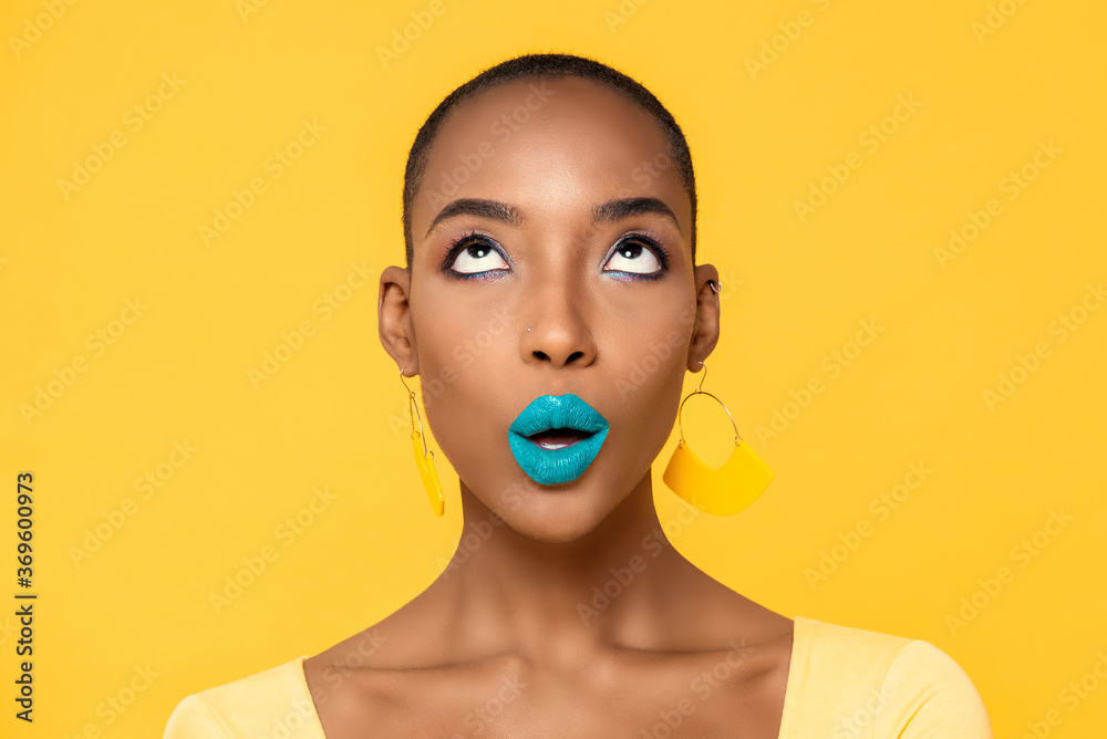 Wall mural Close up portrait of beautiful young African American woman with fashionable colorful make up isolated on yellow studio background