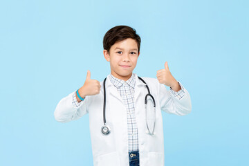Smiling handsome little kid doctor giving double thumbs up isolated on light blue studio background