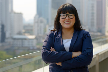Fototapeta premium Happy young beautiful overweight Asian businesswoman against view of the city