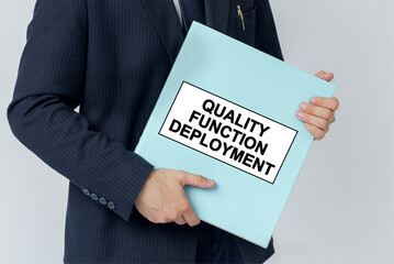 A businessman holds a folder with documents, the text on the folder is - QUALITY FUNCTION DEPLOYMENT