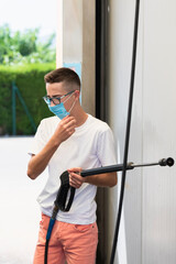 Young man holding a high pressure water spray wand and fixing his surgical mask on an out of focus background. Car wash and safety concept.