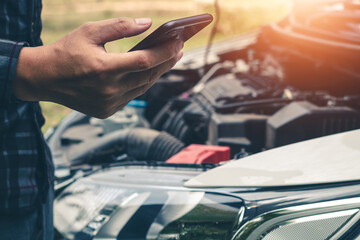 Young man uses a mobile phone to call the mechanic while looking at broken down car on road.