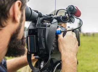 video camera, cameramanon green grass field background.photographer records the sunset in the...