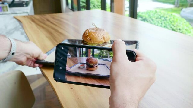 Man Hands Taking Pictures on Mobile Phone of Burger with Beef Cutlet with Melted Cheese, Onion and Tomato Sauce, Rotate and Choose Good Angle for Photo in Restaurant. Concept Unhealthy Food. Closeup