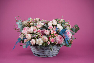 Floral arrangement of roses and peonies in grey wicker basket on a lilac background