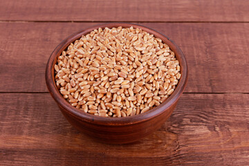 Wheat grains in ceramic bowl on brown wooden table. Top view, high angle, closeup. Harvest, healthy food, ingredient concept