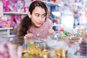 glad schoolgirl delighted with choosing lollipop in candy store